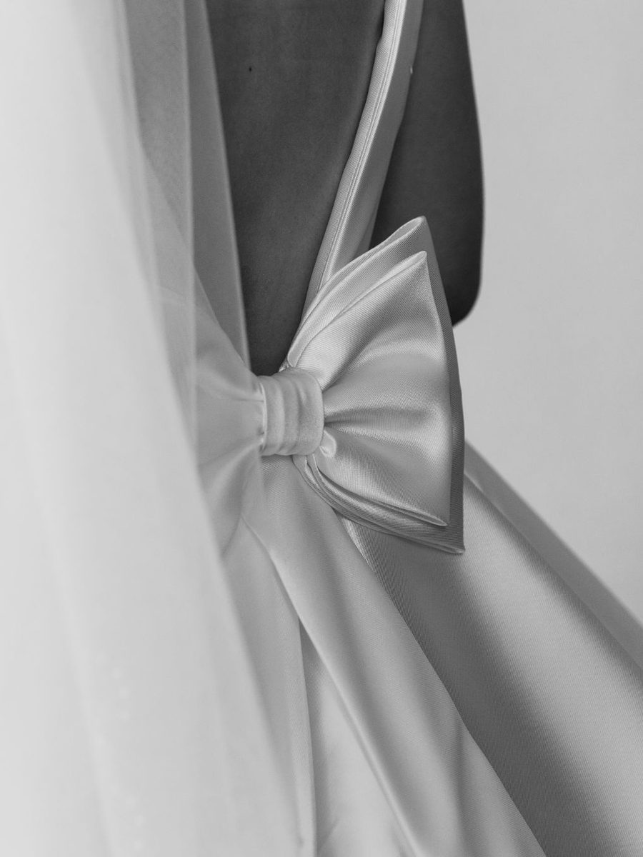 Laço de cetim atado na cintura de um vestido, ao lado do véu, em preto e branco